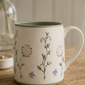 Vit keramikmugg med Julia Sundby af Robsons blomster- och fågelmönster i grönt, rosa och blått